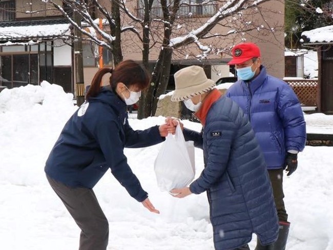 ドローン配送された「ごはんセット」を スタッフから受取る前川さんご夫妻 ドローン配送された「ごはんセット」を スタッフから受取る前川さんご夫妻